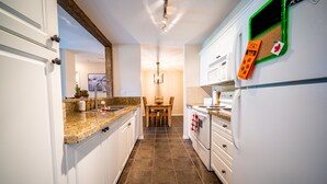 A kitchen with white cabinets, a granite countertop, a dining table with chairs, a stove, and a refrigerator. - 2-Bedroom 2-Bathroom Condo with Mountain Views (Radium Hotsprings)