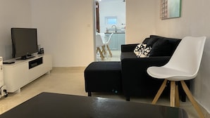 Olohuoneessa on musta sohva, valkoinen tuoli, televisio ja pieni pöytä.