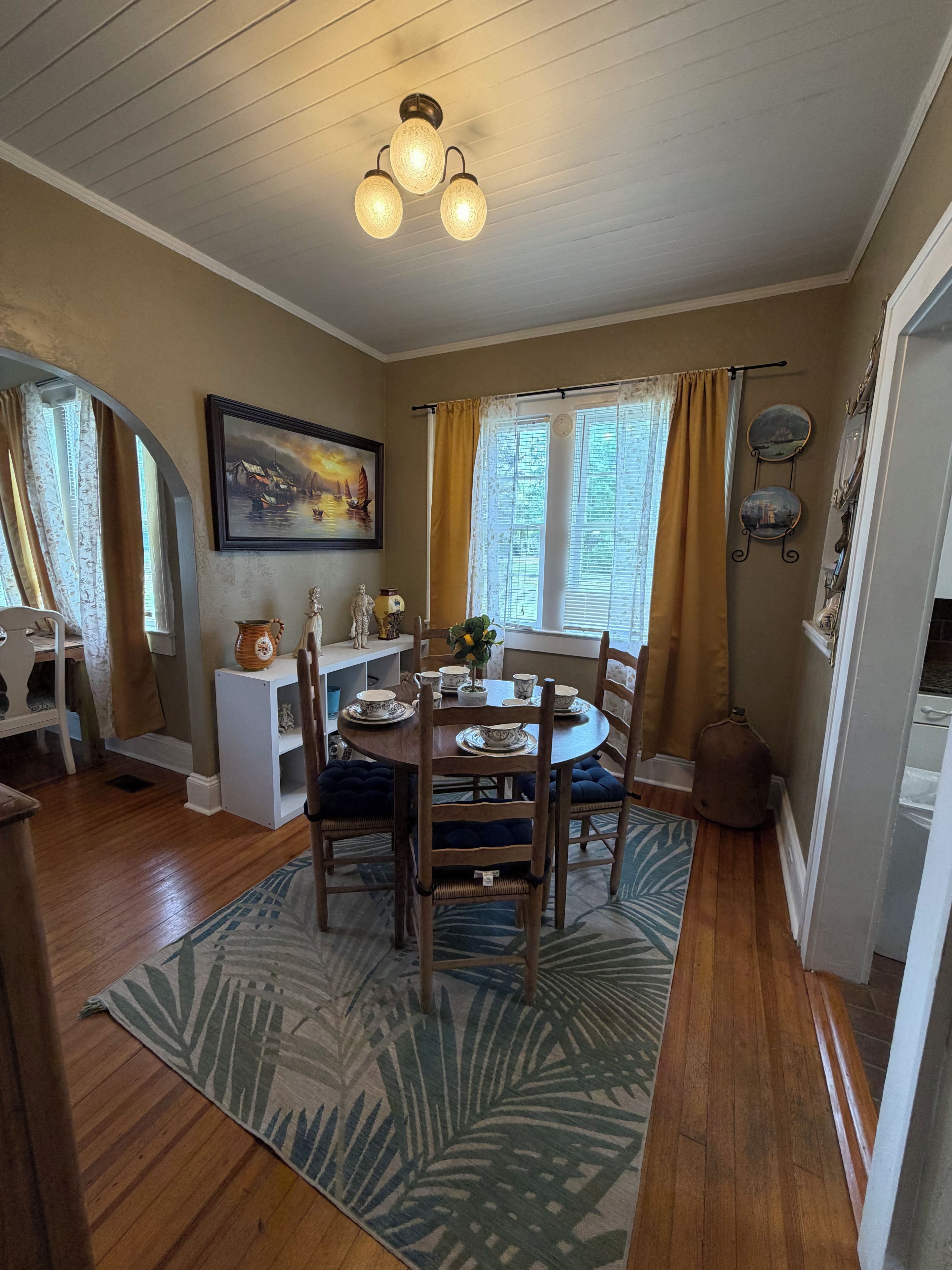 A dining area with a round table, chairs, a patterned rug, and a ceiling light fixture.