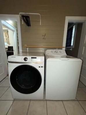 A laundry room with two washing machines, a drying rack, and a wall-mounted shelf.