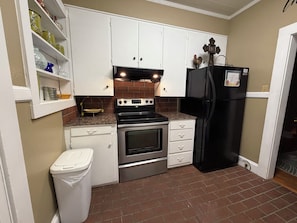 A compact kitchen with white cabinets, a black refrigerator, a stove, and a trash bin. - Spacious 4BR  Sleeps 12+ VSU, SGMC + Parking (Valdosta)