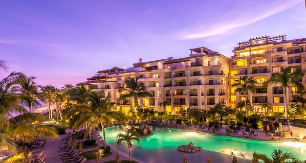 A multi-story hotel with a pool area, palm trees, and outdoor seating.
