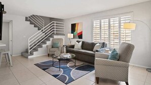 Un salon moderne avec un escalier, un ensemble de canapés, une table basse et une lampe.