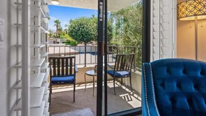 Un balcon avec une chaise bleue, une petite table et une vue sur un paysage verdoyant.