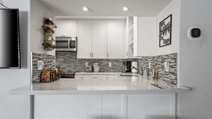 Une cuisine moderne avec des meubles blancs, un îlot central et un revêtement mural décoratif à motifs géométriques.