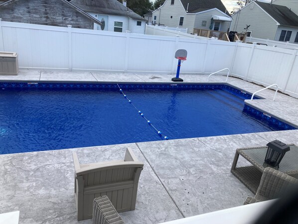 A rectangular swimming pool with a blue interior, surrounded by a white fence.