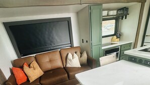 Un espacio habitable compacto con sofá, televisión de pantalla plana, mesa de comedor y kitchenette.