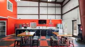 Una cocina amplia con piso a cuadros rojo y negro, una isla grande con taburetes y un televisor de pantalla plana sobre la encimera.