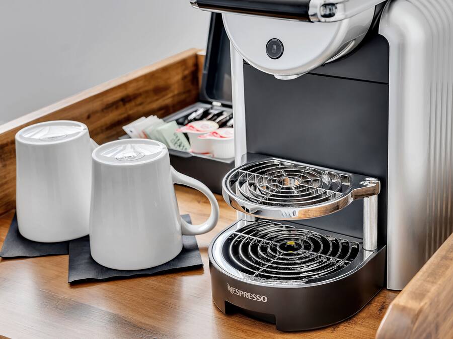 A Nespresso coffee machine with two white mugs on a wooden tray.