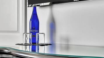 A blue bottle of Sarathoga water, a glass, and a black object on a reflective surface.