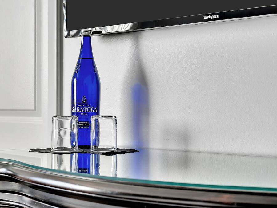 A blue bottle of Sarathoga water, a glass, and a black object on a reflective surface.