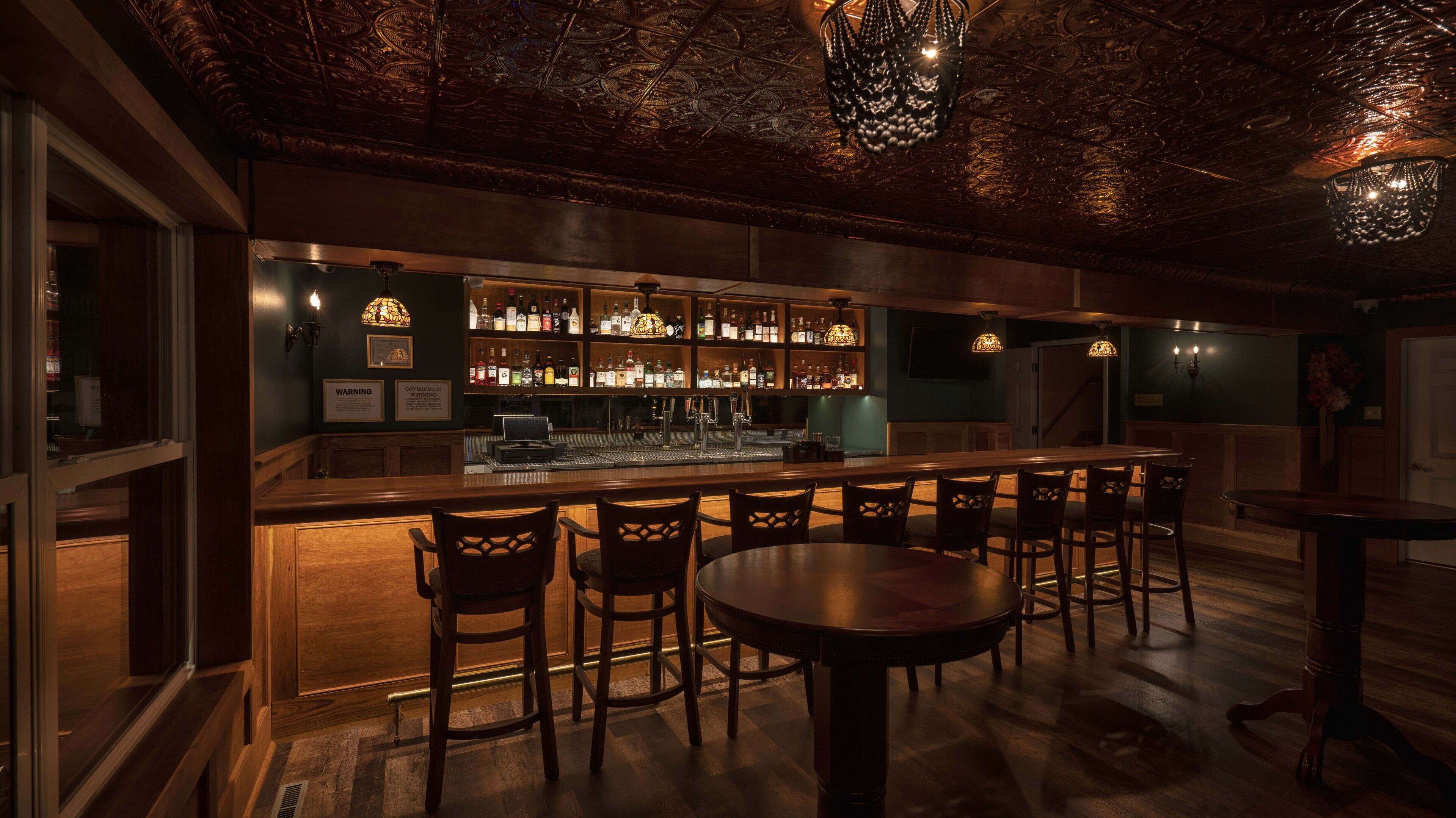 A bar area with wooden furniture, a bar counter, and a variety of bottles.