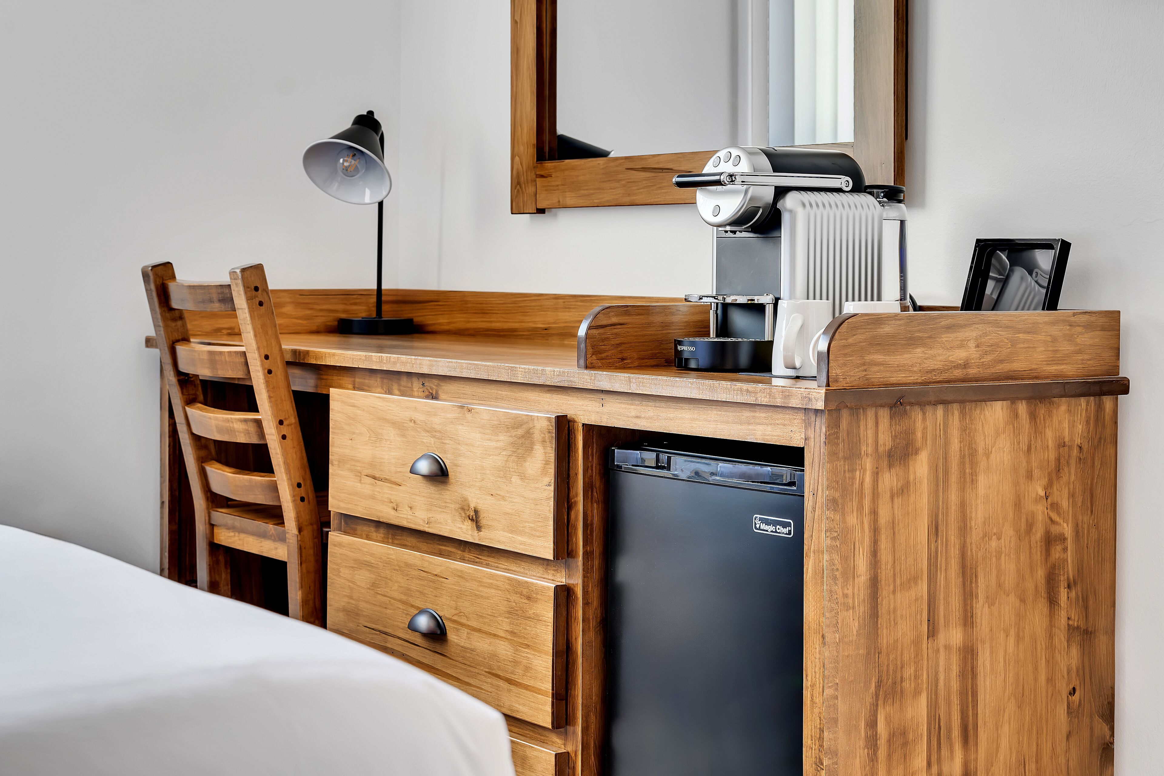 A wooden desk with a coffee machine, a lamp, and a refrigerator.