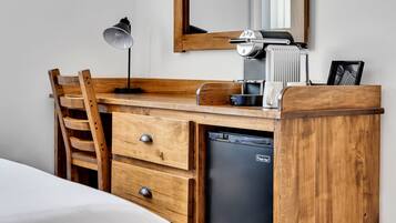 A wooden desk with a coffee machine, a lamp, and a refrigerator.