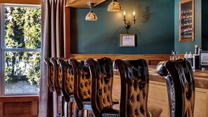 A bar area with leather chairs, a wooden counter, and decorative lighting. - The Inn of Lake George (Lake George)