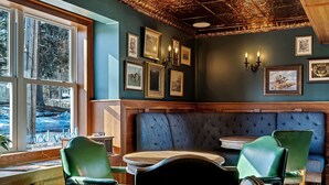 A cozy corner with a blue cushioned bench, green upholstered chairs, and a wooden table. - The Inn of Lake George (Lake George)