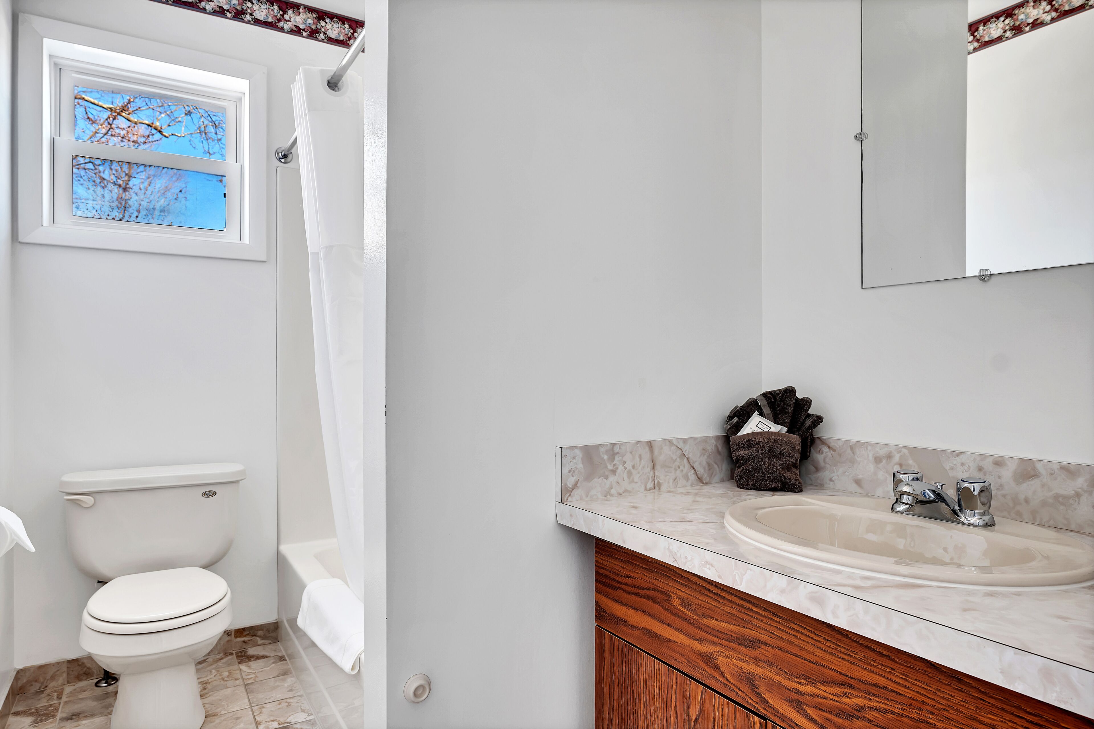 Une salle de bain équipée de toilettes, d’une douche, d’un lavabo et d’une fenêtre donnant sur les arbres.