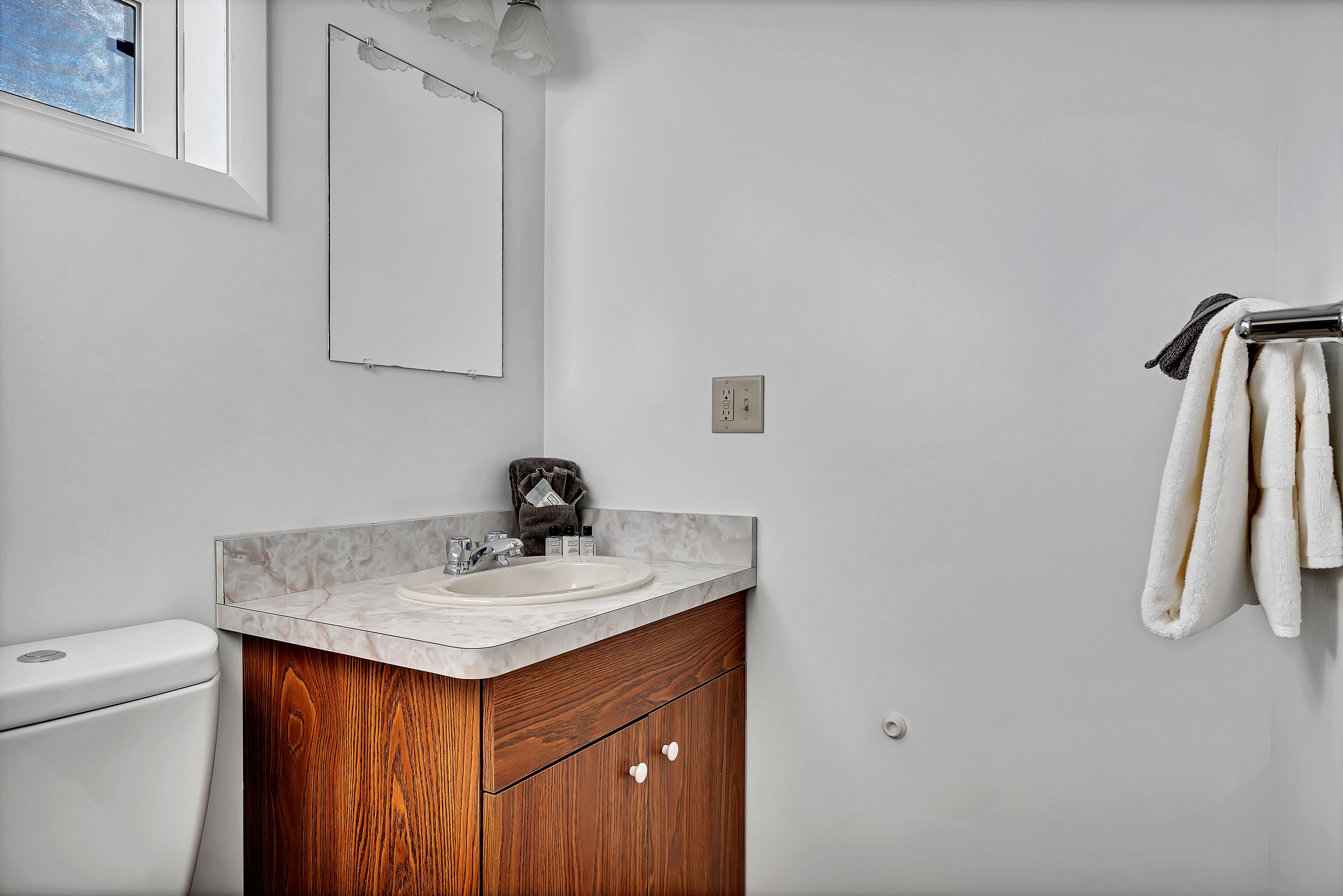 A bathroom with a white toilet, a marble sink vanity, and a towel rack with towels.