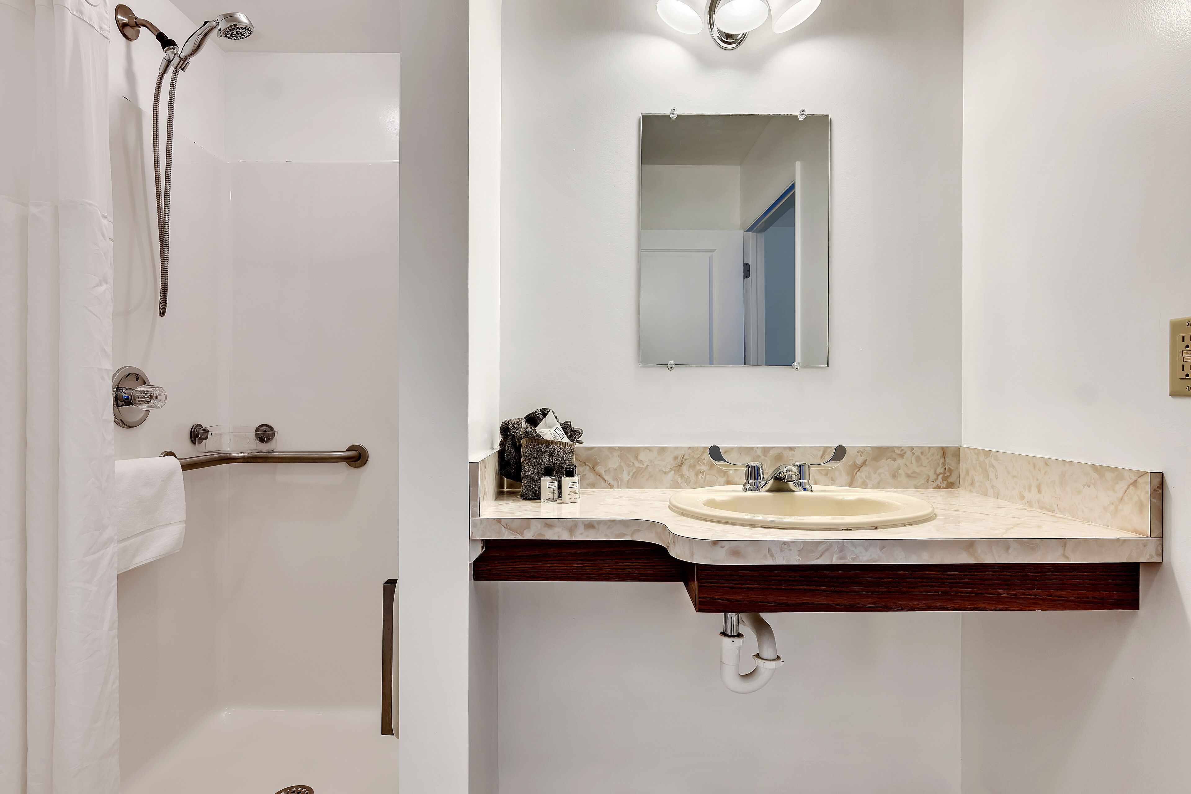 Een badkamer met een witte badkuip, een douche met een handdouche, een wastafel met een spiegel erboven en een handdoekrek.