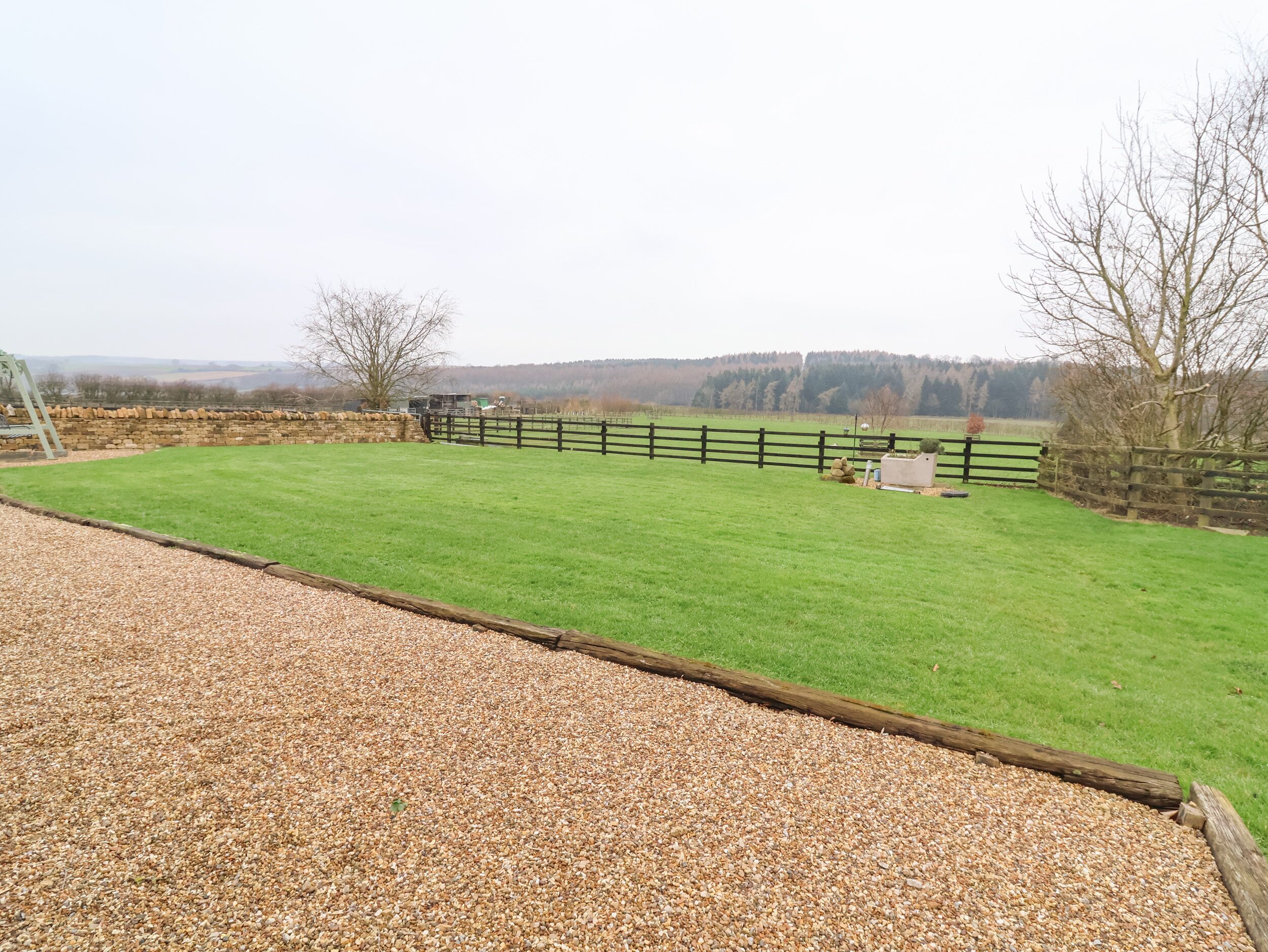 A fenced outdoor area with a gravel path leading to a grassy field.