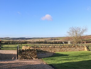 A stone wall and a wooden gate in a rural landscape with a clear sky.