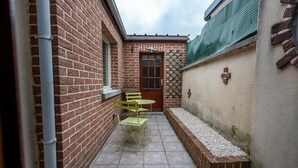 A narrow outdoor patio with a brick wall, a door, and a small seating area with yellow chairs. - La parenthèse amiénoise - Cosysejour (Amiens)