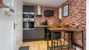 A compact kitchen with modern appliances, a brick accent wall, and a small dining area with stools. - La parenthèse amiénoise - Cosysejour (Amiens)
