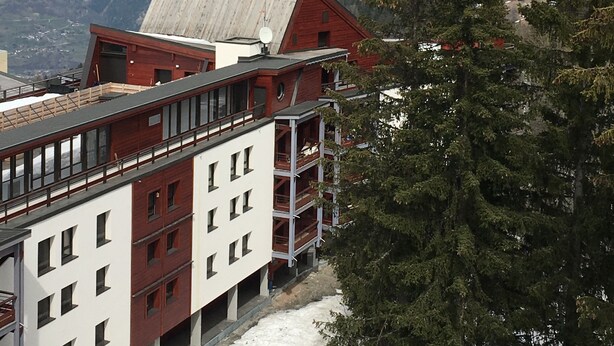 A hotel with a red and white facade, multiple balconies, and a view of snow-capped mountains in the background. - ARC 1800 apartment 6-8pers with garage all comfort (Bourg-Saint-Maurice)