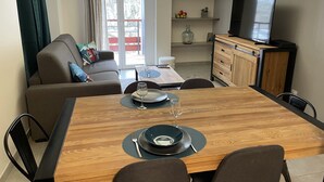 A modern living room with a dining area, a sofa, a TV, and a kitchen area with a cabinet and a shelf. - ARC 1800 apartment 6-8pers with garage all comfort (Bourg-Saint-Maurice)