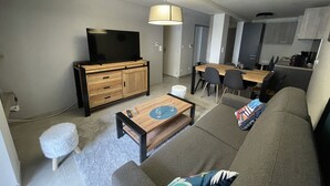 A modern living room with a sofa, coffee table, TV, and dining area. - ARC 1800 apartment 6-8pers with garage all comfort (Bourg-Saint-Maurice)