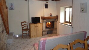 A cozy room with a fireplace, a television on a wooden cabinet, and a bed with a pink and white bedspread. - Combeauté valley 2 to 10pers. (Le Val-d'Ajol)