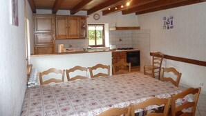 A kitchen with wooden cabinets, a dining table with chairs, and a window with a view of greenery. - Combeauté valley 2 to 10pers. (Le Val-d'Ajol)