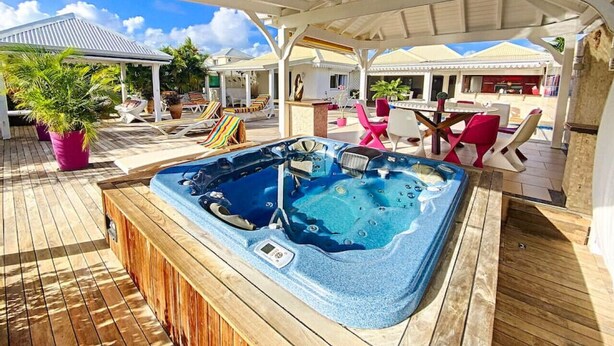 Un espace extérieur abrité comprenant un jacuzzi, des chaises longues et un coin repas.