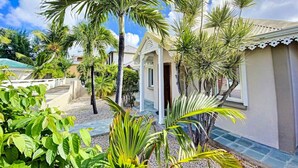 Une maison dotée d’un porche abrité, entourée de palmiers et d’autres plantes vertes.
