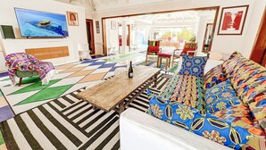 Un salon spacieux avec une grande télévision, des tapis colorés, une table basse en bois et un canapé aux couleurs vives.