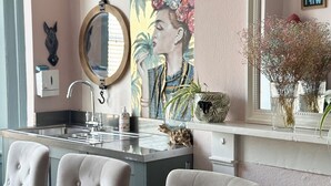 A dining area with a marble table, tufted chairs, a wall-mounted mirror, and a painting.