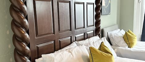 A hotel room with a wooden headboard, two beds with white and yellow pillows, and a wooden nightstand.