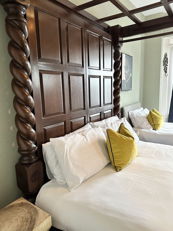 A hotel room with a wooden headboard, two beds with white and yellow pillows, and a wooden nightstand.