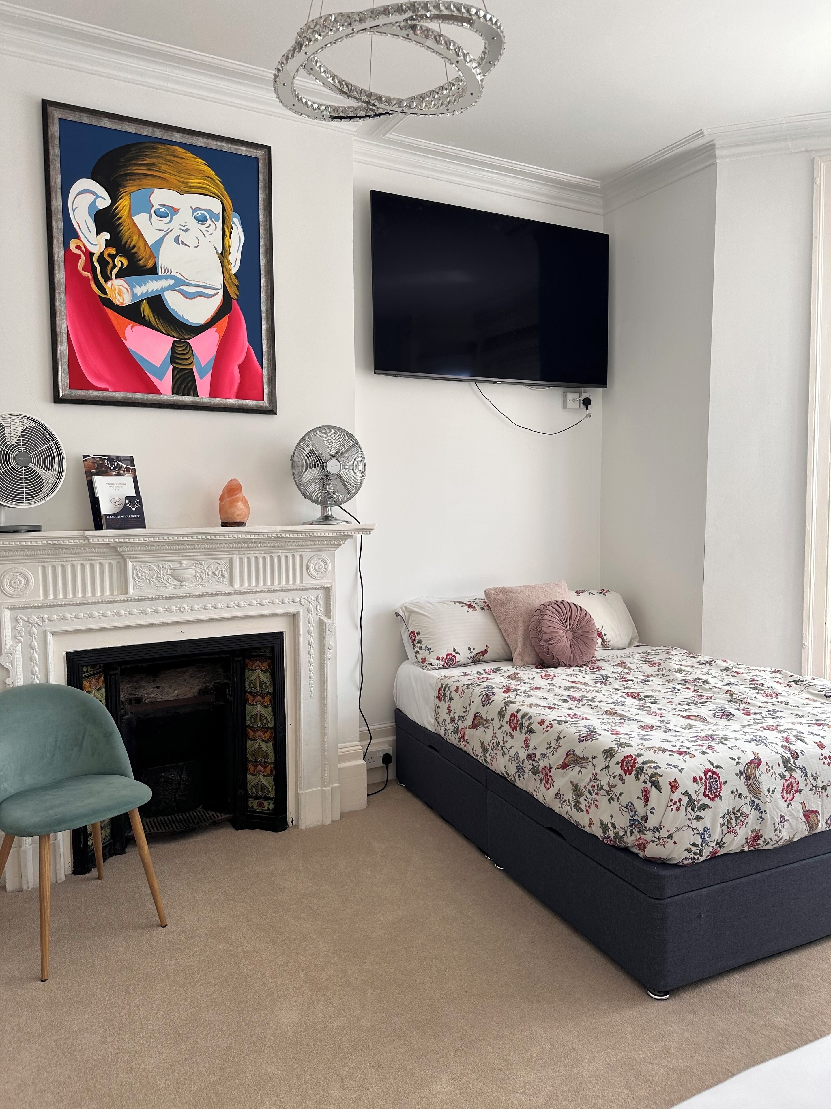 Een slaapkamer met een bed, een televisie, een open haard, een ventilator en een schilderij.