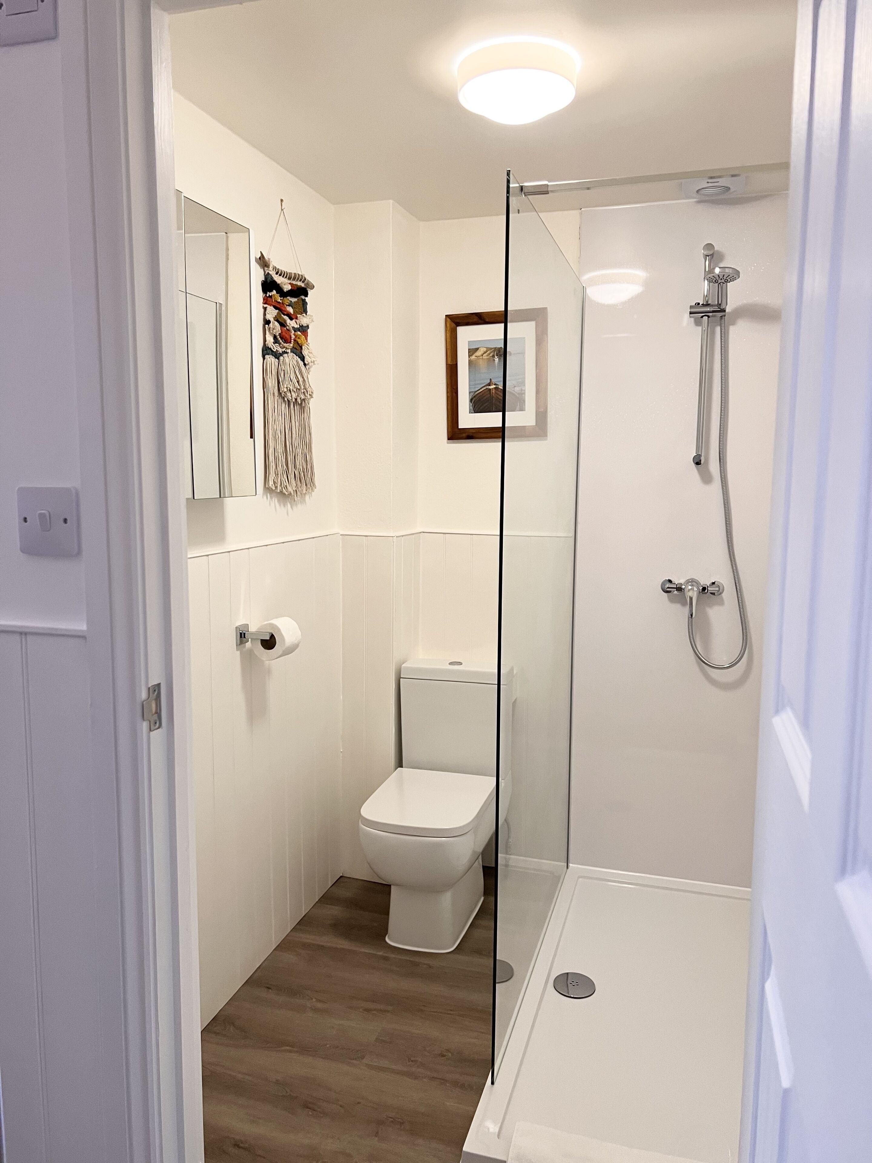 Un baño con inodoro, ducha con puerta de vidrio y un cuadro en la pared.