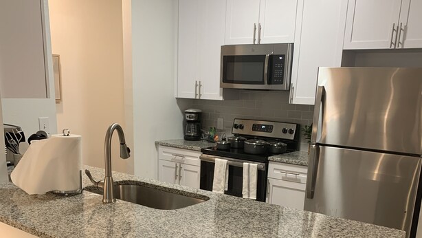 A modern kitchen with white cabinets, a granite countertop, stainless steel appliances, and wooden stools. - Fabulous 3 bedroom/2 bath with attached Garage (Alpharetta)