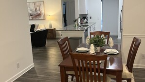 A dining area with a wooden table and chairs, a kitchen in the background, and a patterned rug on the floor. - Fabulous 3 bedroom/2 bath with attached Garage (Alpharetta)