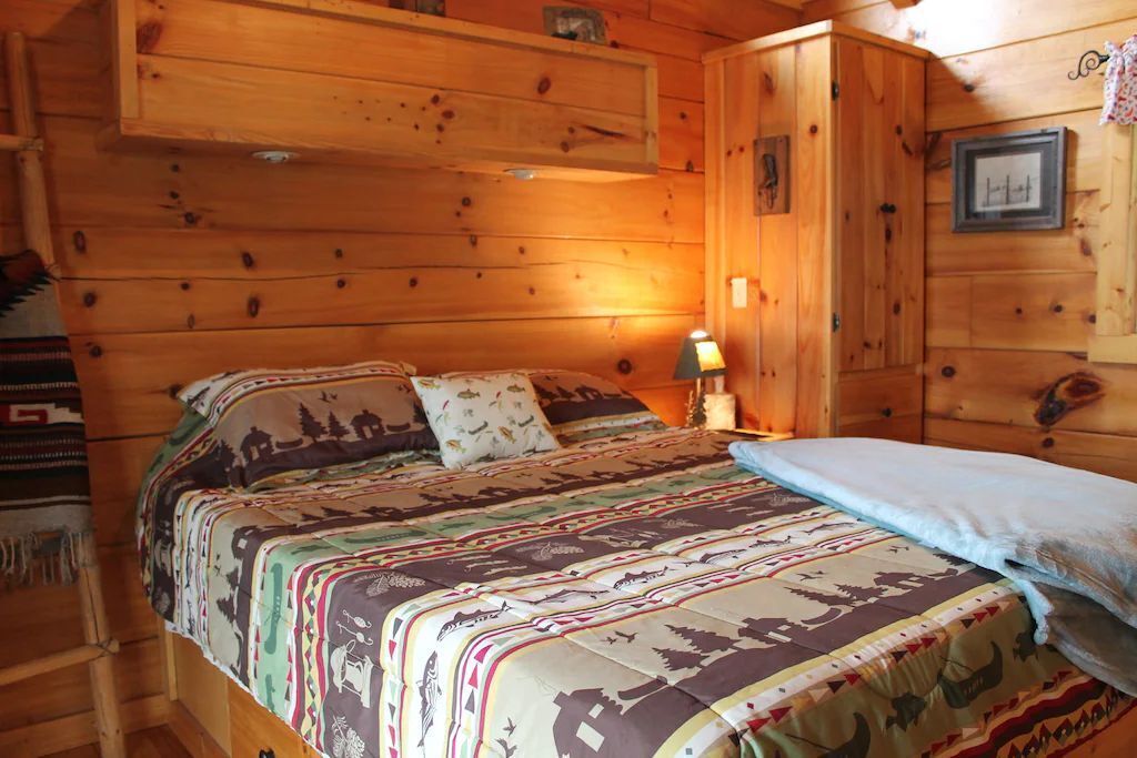 Quarto de cabana de madeira com uma cama, uma mesa de cabeceira e um armário fixado na parede.