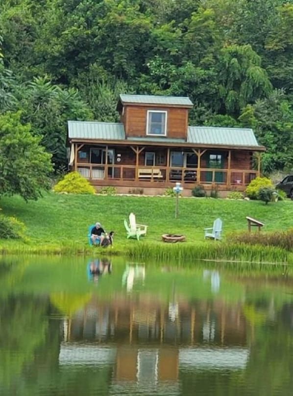 Eine Holzhütte mit Metallbedachung, umgeben von üppigem Grün und einem Teich.
