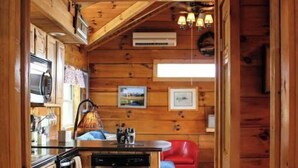 Interior de una cabaña de madera con cocina, comedor y una silla roja.