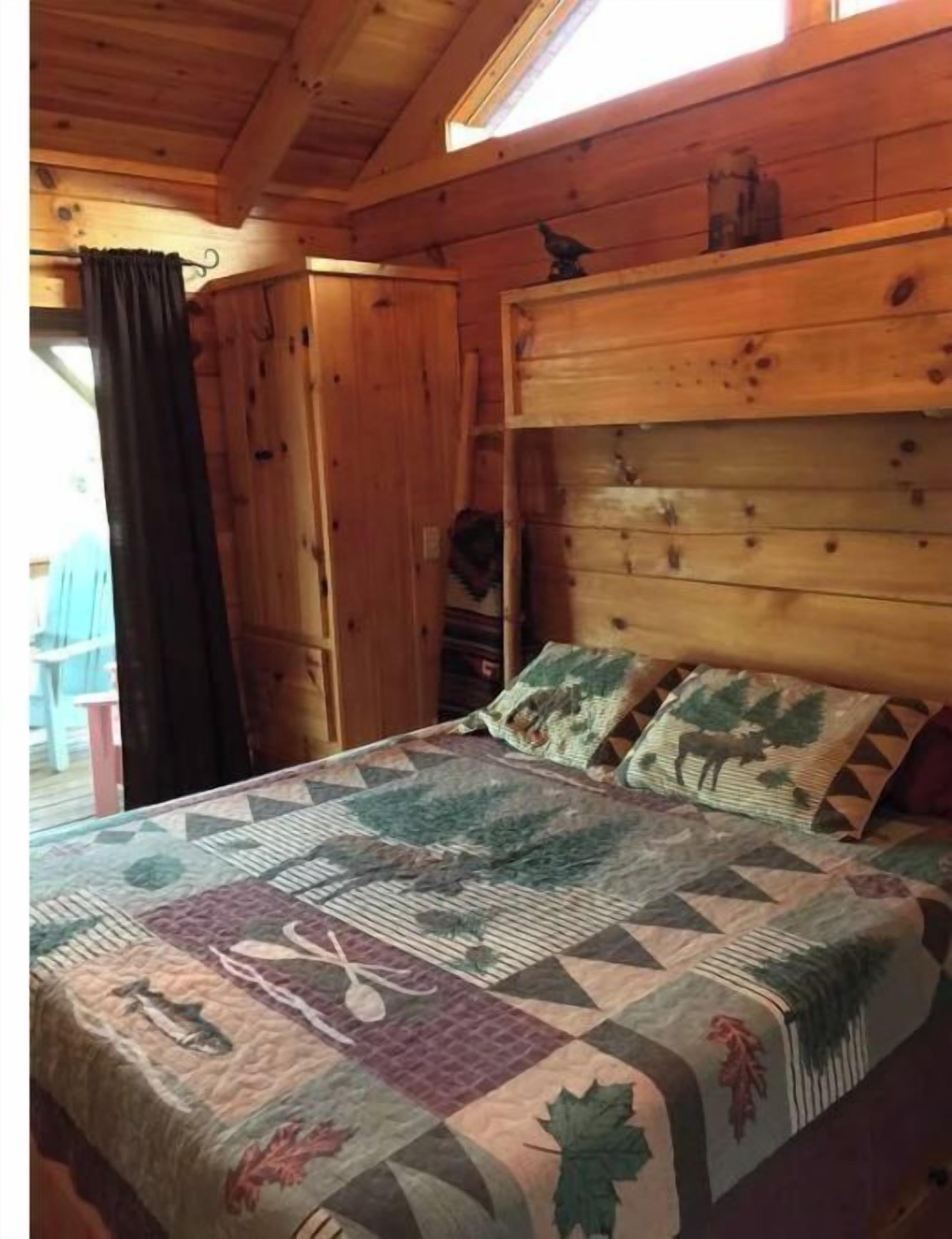 A wooden cabin bedroom with a bed, a window, and a door.