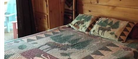 A wooden cabin bedroom with a bed, a window, and a door.