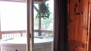 Una habitación con una cama de madera, un ventanal de vidrio que da a un jacuzzi y una terraza de madera afuera.
