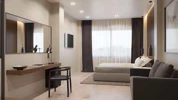 A modern hotel room with a bed, a sofa, a desk with a chair, a large mirror, and a flat-screen TV.