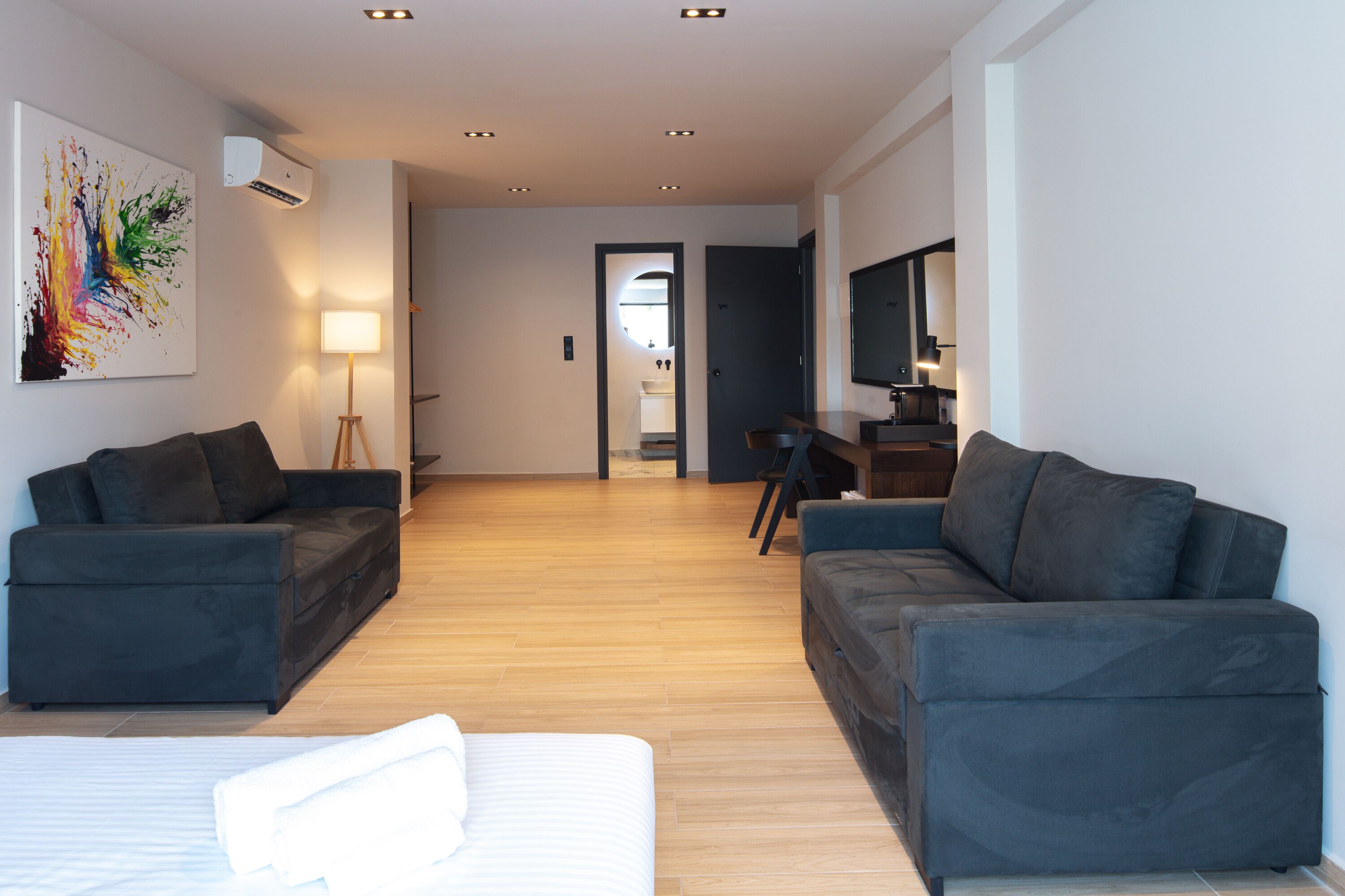 A modern living room with two dark sofas, a white bed, and a wooden floor.